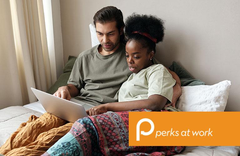 Couple sitting on a bed looking at a computer